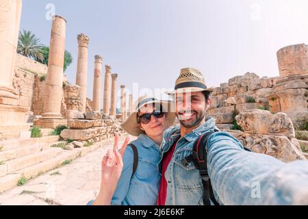Ein junges Paar mit Hut nimmt ein Selfie und genießt an einem sonnigen Tag die wunderschöne Landschaft der antiken Ruinen von Jerash Stockfoto