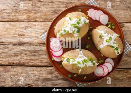 Gekochte Mantelkartoffeln, gefüllt mit Quark, Sauerrahm und grünen Zwiebeln, in der Nähe auf einem Teller auf einem Holztisch. Horizontale Draufsicht von oben Stockfoto