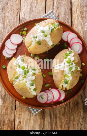 Auf einem Teller auf einem Holztisch Kartoffeln mit gesalzenem Quark und grünen Zwiebeln in der Nähe schälen. Vertikale Draufsicht von oben Stockfoto
