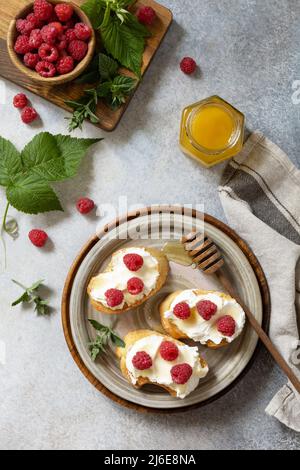 Gesundes Sommerfrühstück mit süßen Sandwiches mit Ricotta, Himbeeren und Honig auf einem Steintisch. Draufsicht flach liegend. Stockfoto