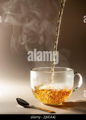 Tee wird in Glas-Teetasse mit Dampf auf braunem monochromen Hintergrund gegossen Stockfoto