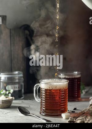 Stillleben mit schwarzem Tee in Glas gegossen. Mit Dampf. Bereiten Sie Tee zu. Selektiver Fokus Stockfoto