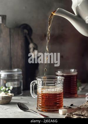 Stillleben mit schwarzem Tee in Glas gegossen. Mit Dampf. Bereiten Sie Tee zu. Selektiver Fokus Stockfoto