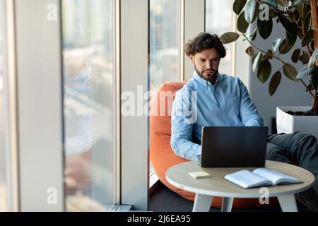 Ein Geschäftsmann, der im Büro einen Laptop benutzt, sitzt auf einem Stuhl Stockfoto