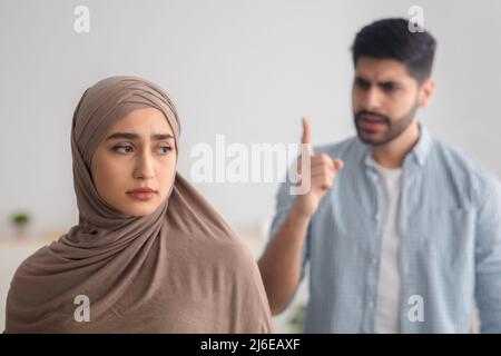 Wütender Muslimischer Mann, Der Depressive Ehefrau Anbrüllt, Die Einen Konflikt In Der Halle Hat Stockfoto