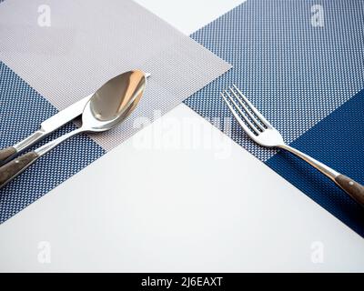 Gabel, Löffel und Messer mit leerem Platz auf dem blauen Tischset auf dem weißen Tisch für die Gäste im Frühstücksraum des Hotels. Stockfoto