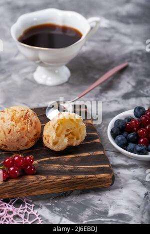 Kleine weiße Brötchen mit frischen Beeren mit einer Tasse Kaffee auf einem grauen Betonhintergrund. Stockfoto