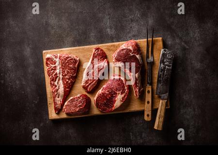 Set aus verschiedenen klassischen, alternativen rohen Fleischsteaks auf Schneidebrett über Stein Hintergrund Stockfoto