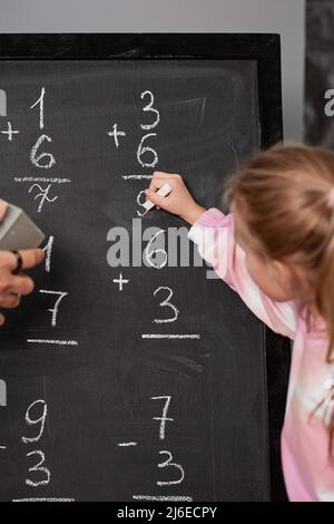 Mädchen, die mathematische Lösung auf die Tafel schreiben, während sie Zahlen im Schulunterricht zählen Stockfoto