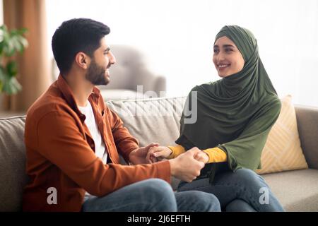 Glückliches Paar Aus Dem Nahen Osten, Das Die Hände Hält Und Zu Hause Sitzt Stockfoto