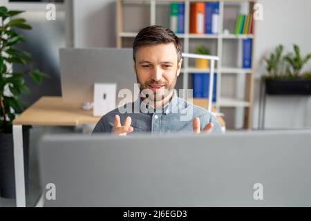 Ein positiver, reifer Geschäftsmann, der während des Videoanrufs in einem modernen Büro zur Webkamera gestikelt wird Stockfoto