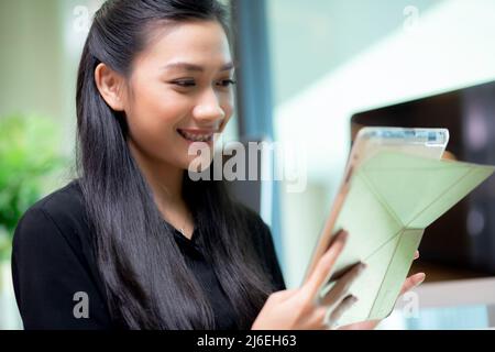 Junge asiatische Geschäftsfrau mit Tablet-Computer arbeiten im Büro, Frau oder Mitarbeiter suchen Tablet mit selbstbewussten, Geschäftsleute arbeiten online, ein Stockfoto