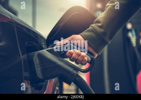 Kaukasische Männer laden sein Elektrofahrzeug an der Ladestation Close Up Foto. Stockfoto