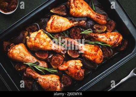 Gebackene Hähnchenbeine, Drumsticks mit süßen Feigen und Zwiebeln in balsamischer Marinade auf schwarzem Backblech, rostiger grüner Tischhintergrund, Draufsicht Stockfoto