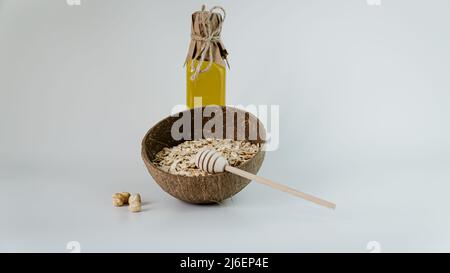 Haferflocken in Bambusschüssel und Honig mit Holzstab auf weißem Hintergrund mit Nüssen. Stockfoto