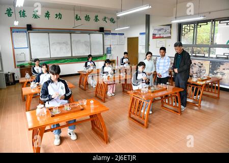 (220501) -- MEITAN, 1. Mai 2022 (Xinhua) -- Guo Jun (2. R) und sein Lehrer Liu Xiaohua (1. R) beobachten einen Studenten, wie er Tee in einer örtlichen technischen Schule im Bezirk Meitan, südwestlich der Provinz Guizhou, zubereitet, 29. April 2022. Guo Jun ist damit beschäftigt, Teeblätter auf einem Herd zu toasten und sonnt sich in dem frischen Aroma, das einen Workshop im Bezirk Meitan füllt. Nach seinem Abschluss an der Universität Guizhou im Jahr 2016 kehrte Guo in seine Heimatstadt zurück, um bei einer Teegesellschaft zu arbeiten, wo er von einem lokalen Meister Tee zubereiten lernte. 2018 wurde er zwei Jahre später Lehrer an einer örtlichen technischen Schule. Die Fähigkeit, Tee zu machen, zu verbessern, ist gefragt Stockfoto