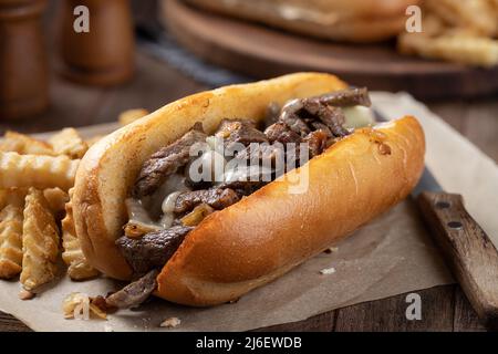 Philly Cheesesteak-Sandwich mit Steak, Käse und Zwiebeln auf einer gerösteten hoagie-Rolle mit pommes auf einem Holztisch Stockfoto