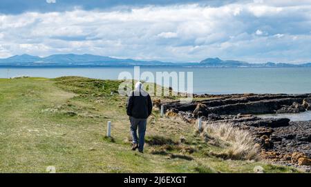 East Lothian, Schottland, Vereinigtes Königreich, Mai 1. 2022. Wetter in Großbritannien: Sonnenschein an der East Lothian Coast. Ein älterer Mann spaziert entlang der Küste des Firth of Forth mit Blick auf die Skyline von Edinburgh und die Pentland Hills in der Ferne Stockfoto