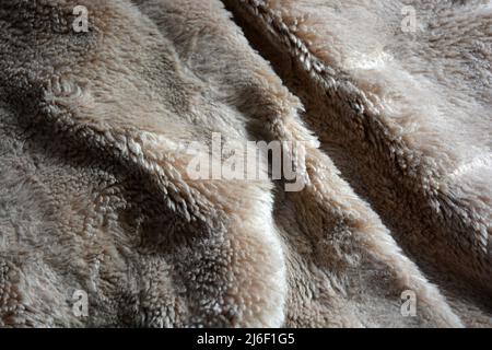 Synthetisches braunes Material in Form von Naturwolle, natürliches, teures Naturpelz. Ungewöhnlicher beigefarbener, fleischfarbener Pelzhintergrund. Stockfoto