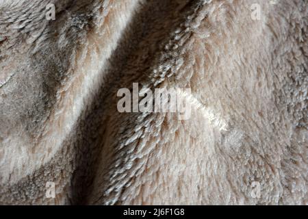 Synthetisches braunes Material in Form von Naturwolle, natürliches, teures Naturpelz. Ungewöhnlicher beigefarbener, fleischfarbener Pelzhintergrund. Stockfoto