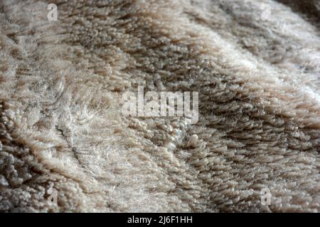 Synthetisches braunes Material in Form von Naturwolle, natürliches, teures Naturpelz. Ungewöhnlicher beigefarbener, fleischfarbener Pelzhintergrund. Stockfoto