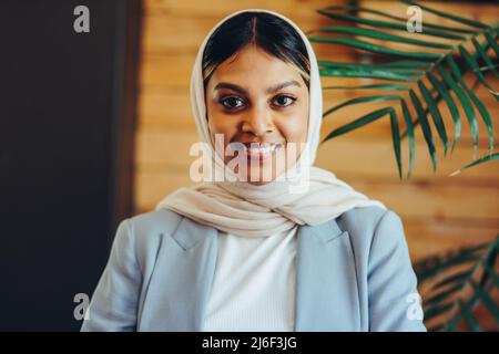 Porträt einer muslimischen Geschäftsfrau, die die Kamera anschaut, während sie einen Hijab trägt. Glückliche Unternehmerin, die an einem integrativen Arbeitsplatz arbeitet. Stockfoto