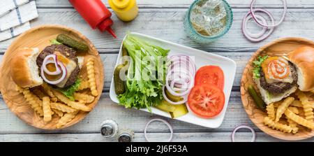 Eine schmale Ansicht der Cheeseburger-Schieberegler mit einer Platte von Belägen in der Mitte. Stockfoto