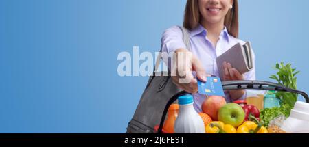 Frau, die einen vollen Warenkorb hält und mit einer Kreditkarte für Lebensmittel bezahlt Stockfoto