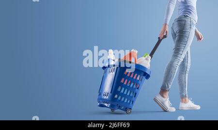 Frau, die einen Einkaufskorb mit Reinigungsprodukten und leerem Kopierbereich zieht Stockfoto