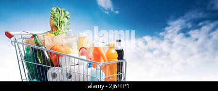 Warenkorb gefüllt mit Waren und blauer Himmel im Hintergrund, Lebensmitteleinkaufkonzept Stockfoto