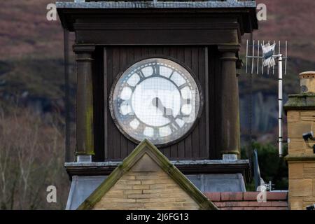 Weißes Zifferblatt auf einem Uhrturm mit römischen Ziffern und dem Minutenzeiger, der den Stundenzeiger überlappt, West Yorkshire, England, Großbritannien Stockfoto