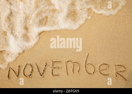 November - handgeschrieben auf dem weichen Strandsand. Stockfoto