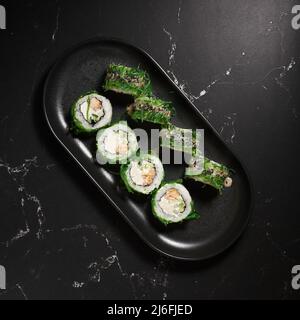 Grünes Sushi. Japanisches Sushi mit Chuka-Salat auf schwarzem Stein, selektiver Fokus. Japanische Küche. Sushi-Menü. Asiatische Ernährung. Draufsicht. Stockfoto