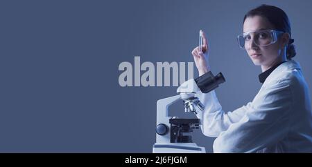 Junger Wissenschaftler mit einem Reagenzglas und einem Mikroskop, Medizin und wissenschaftlichen Forschungskonzept Stockfoto