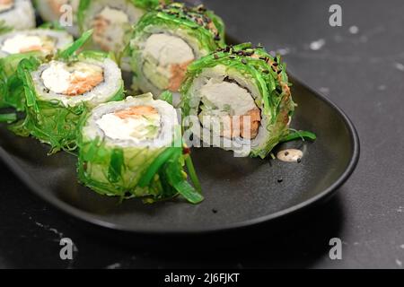 Grünes Sushi. Japanisches Sushi mit Chuka-Salat auf schwarzem Stein, selektiver Fokus. Japanische Küche. Sushi-Menü. Asiatische Ernährung. Nahaufnahme Stockfoto