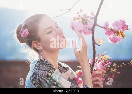 Weiße Frau im Sonnenlicht hält Kirschbaumblüte im Frühling, Weiblichkeit Stockfoto
