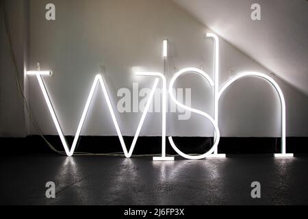 Ein großes „Wish“-Schild in einem dunklen Zimmer mit weißen Wänden und grauem Boden. Stockfoto