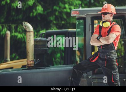 Professioneller kaukasischer Raupenfahrer oder Bulldozer-Fahrer in seinem 30s. Aufenthalt in der Nähe von Schwermaschinen Stockfoto