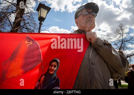 Moskau, Russland. 1.. Mai 2022. Ein Mann hält ein Transparent mit einem Porträt der ukrainischen Babuschka mit sowjetischer Flagge während einer Kundgebung der Anhänger der Kommunistischen Partei Russlands anlässlich des Internationalen Arbeitertages auf dem Teatralnaja-Platz im Zentrum von Moskau, Russland. Die Oma mit dem Roten Banner, eine ältere Frau, die auf einem Video festgehalten wurde, begrüßte ukrainische Militärangehörige mit einem sowjetischen Roten Banner und verwechselte sie mit Russisch Stockfoto