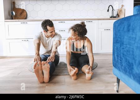 Lächelndes junges sportliches Paar, das Yoga-Unterricht praktiziert, dabei nach oben schauende Hundeübung macht, Urdhva mukha shvanasana Pose, Workout, Indoor voller Länge Stockfoto