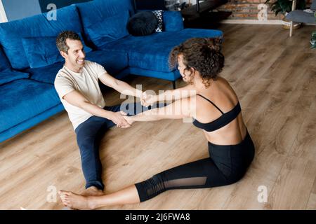 Fit Frau und Mann in Sportbekleidung machen Yoga auf dem Boden Zu Hause mit Laptop hält Tutorial, winkt hallo zu students.Female männlich Coaches haben eine virtuelle Stockfoto