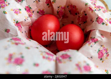 Zwei rot gefärbte Ostereier in einer Schüssel mit geblümten Papierservietten. Stockfoto