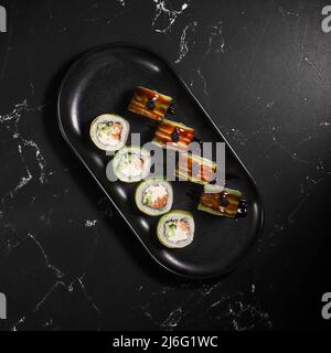 Grüner Drache. Uramaki Sushi-Rolle mit geräuchertem Aal-Unagi, bedeckt mit Avocado auf schwarzem texturierten Hintergrund. Sushi-Menü. Japanisches Essen. Nahaufnahme Stockfoto