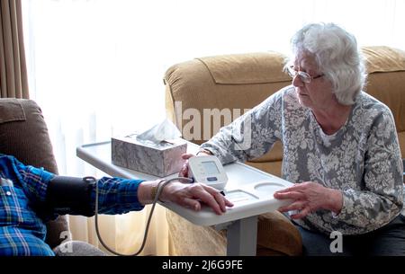 Eine ältere Frau überprüft den Blutdruck ihres Mannes zu Hause Stockfoto