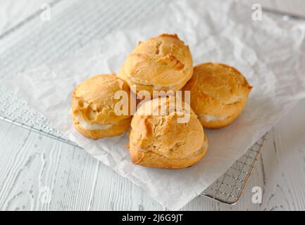 Hausgemachte Profiterolen oder Ecolirs auf einem Metallgitter auf einem hellen Holzhintergrund. Klassisches französisches Dessert. Nahaufnahme. Stockfoto