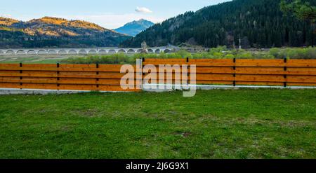 Zaun und grünes Gras in der Natur. Poiana Teiului Viadukt im Hintergrund, Rumänien Stockfoto