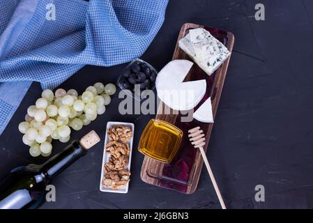 Draufsicht auf eine Vorspeise mit verschiedenen Blauschimmelkäse und Camembert auf einem Holzbrett mit Honig und Trauben und einer Flasche Wein Stockfoto