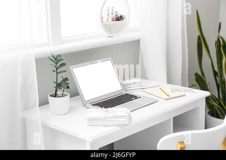 Arbeitsplatz mit modernem Laptop und Buchstaben in der Nähe des Fensters im Zimmer Stockfoto