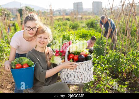 Lächelndes Mädchen und ihre Mutter stehen mit Ernte im Gemüsegarten Stockfoto