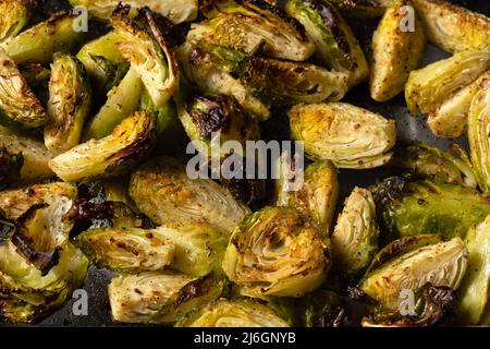 Brüsseler Rosenkohl, gebraten im Ofen mit Gewürzen, Salz, schwarzem Pfeffer und italienischen Kräutern in einer Glasschale. Vegetarisches Hausmannskonzept. Stockfoto